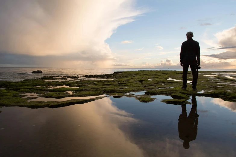 a person standing in front of a body of water, inspired by Storm Thorgerson, rock pools, gazing off into the horizon, infinite reflections, marsden