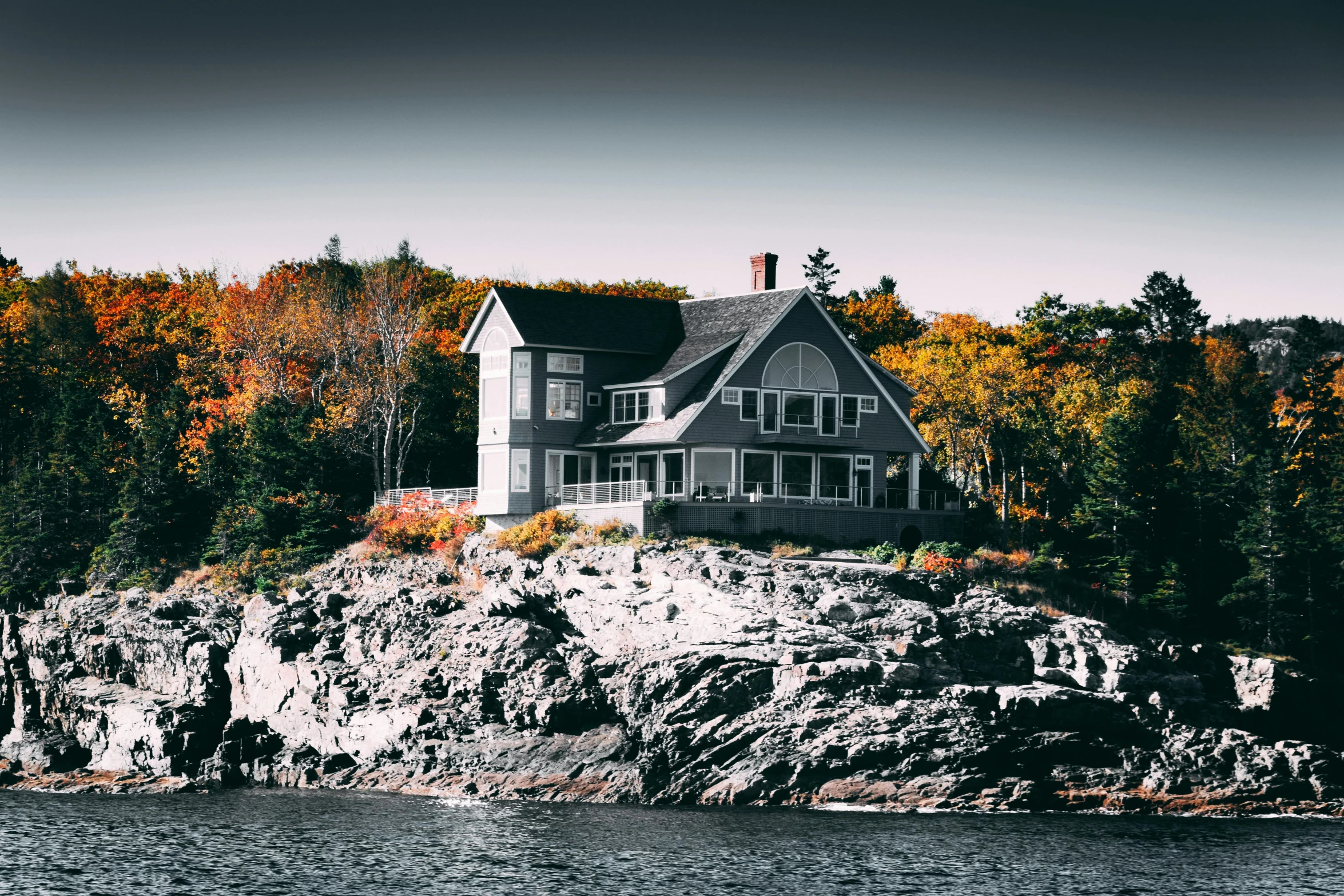 a house sitting on top of a cliff next to a body of water, by Carey Morris, pexels contest winner, cottage decor, contrasted colors, mid fall, grey