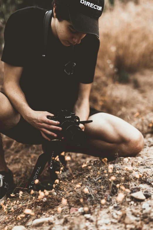 a man kneeling down while holding a camera, inspired by Elsa Bleda, unsplash, wearing black shorts, trail camera, in the grass, rugged details