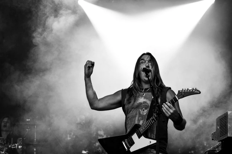 a man holding a guitar on top of a stage, a black and white photo, by Kristian Zahrtmann, pexels contest winner, figuration libre, iron maiden, with red haze and a massive grin, [ metal ], elevation