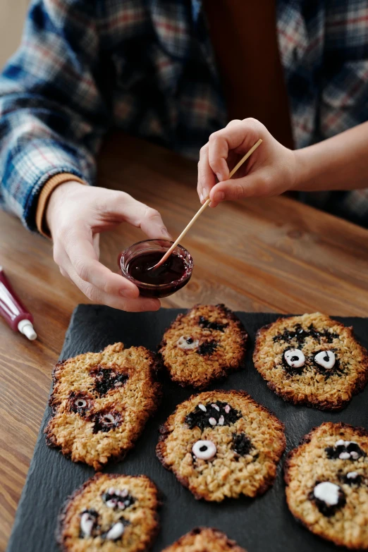 a person holding a toothpick over a tray of cookies, inspired by Mārtiņš Krūmiņš, with haunted eyes and curly hair, squashed berry stains, recipe, kids