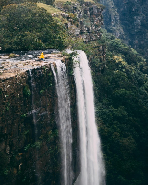 a man standing on top of a cliff next to a waterfall, south african coast, angel sitting on a rock, yellow, top selection on unsplash