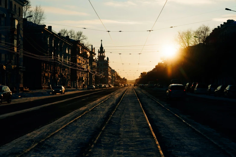 a train traveling down a train track next to tall buildings, by Kristian Zahrtmann, pexels contest winner, winter sun, street tram, early evening, ground level view of soviet town