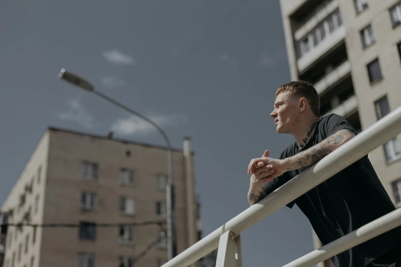 a man leaning on a railing in front of a building, by Attila Meszlenyi, pexels contest winner, vitalik buterin, looking into the distance, people with mohawks, 15081959 21121991 01012000 4k