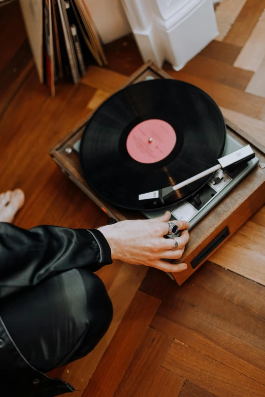 a man sitting on the floor next to a record player, by Everett Warner, trending on pexels, on a wooden tray, spinning hands and feet, a man wearing a black jacket, vibrating