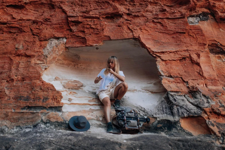 a woman sitting on a rock looking at her cell phone, a cave painting, by Lee Loughridge, pexels contest winner, aboriginal australian hipster, sandstone, having a snack, letterboxing