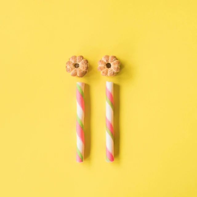 two candy sticks sitting next to each other on a yellow background, trending on pexels, op art, pink yellow flowers, earring design, donut, torches on wall