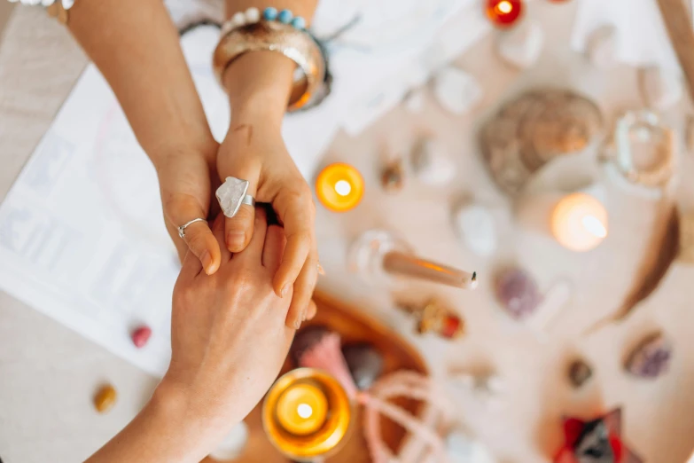 a man and a woman holding hands over a table with candles, by Julia Pishtar, trending on pexels, crystals and diamonds, woman holding another woman, chakras, on a white table