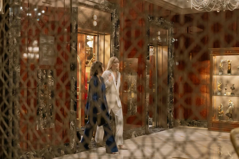 a couple of people that are walking in a room, pexels, art nouveau, behind bars, people shopping, blonde, gold and white robes