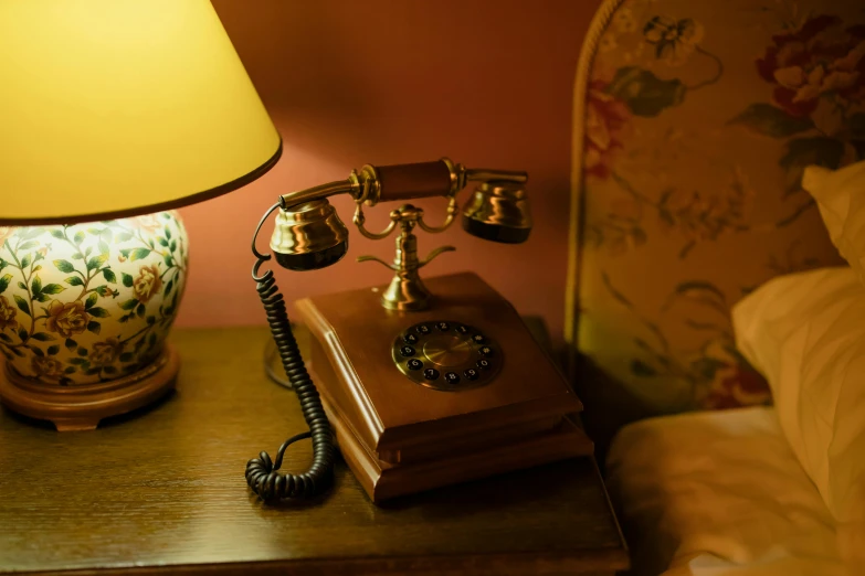 a telephone sitting on top of a wooden table next to a lamp, inspired by Clarice Beckett, gold, from the grand budapest hotel, brown, hotel room