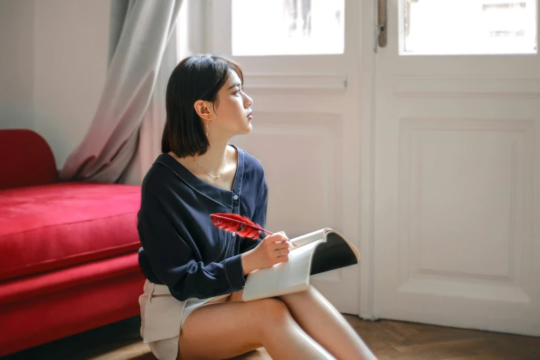 a woman sitting on the floor in front of a red couch, pexels contest winner, realism, drawing pictures on a notebook, beautiful south korean woman, wearing shorts and t shirt, girl wearing uniform