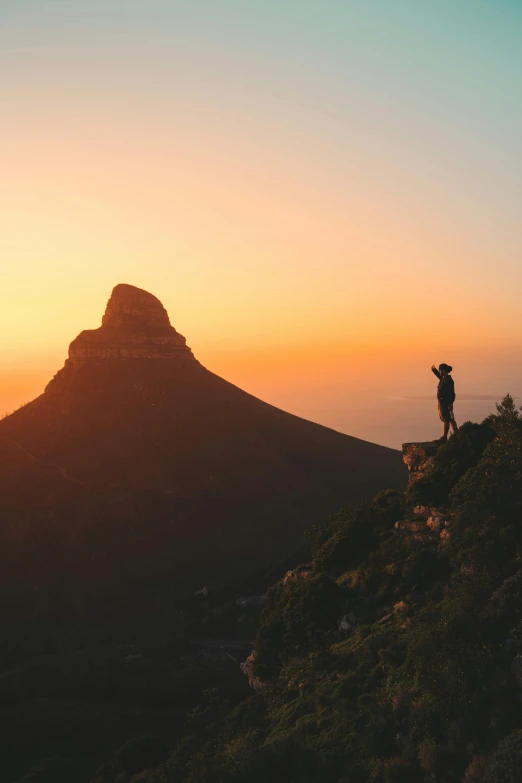 a person standing on top of a mountain at sunset, south african coast, surrounding the city, 2019 trending photo, small in size