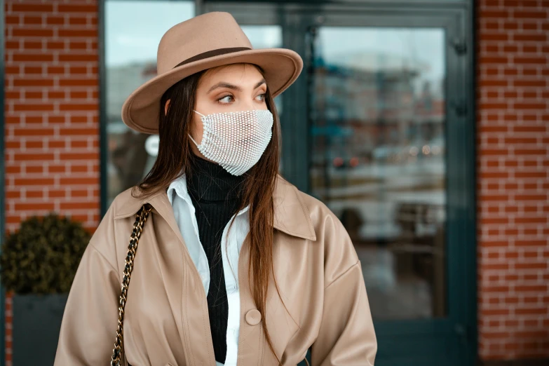 a woman wearing a face mask in front of a building, trending on pexels, light brown trenchcoat, caracter with brown hat, neoprene, see - through