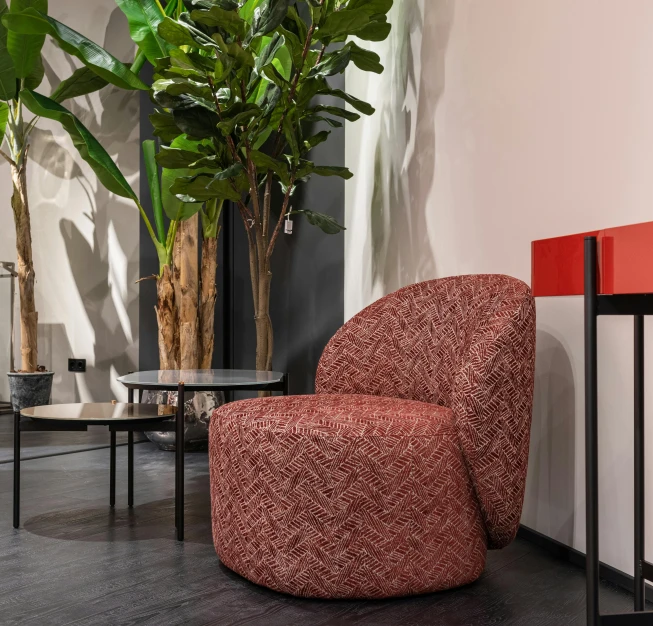 a red chair sitting in a living room next to a plant, inspired by Vito D'Ancona, herringbone floor, rounded architecture, red fabric, vtm