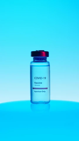 a bottle of liquid sitting on top of a blue surface, a picture, by Josh Bayer, shutterstock, medical labels, beauty is a virus, covid, syringe