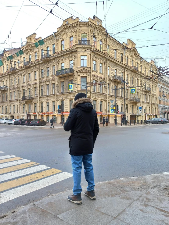 a person standing on a sidewalk in front of a building, inspired by Illarion Pryanishnikov, pexels contest winner, panorama view, facing away from the camera, hidden camera photo, square