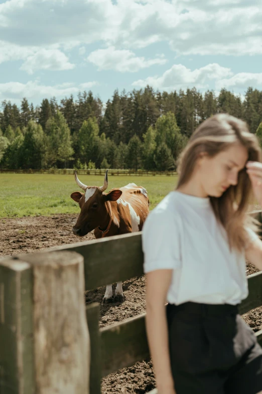 a woman standing in front of a fence next to a cow, by Anna Boch, pexels contest winner, photo of young woman, 🐎🍑, low quality footage, nordic summer