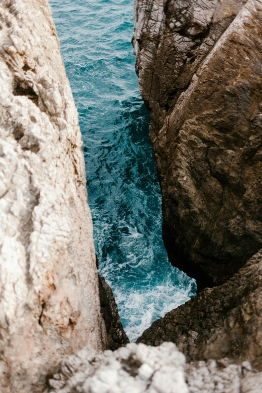 a man standing on top of a rock next to the ocean, by Niko Henrichon, trending on unsplash, renaissance, marble hole, close-up from above, grotto, ((rocks))