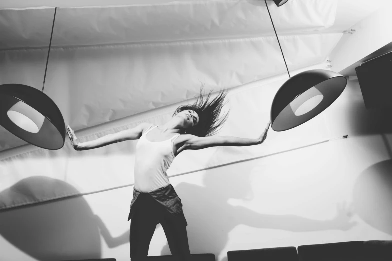 a black and white photo of a woman jumping in the air, light and space, things hanging from ceiling, spinning, low quality photo, trending photo