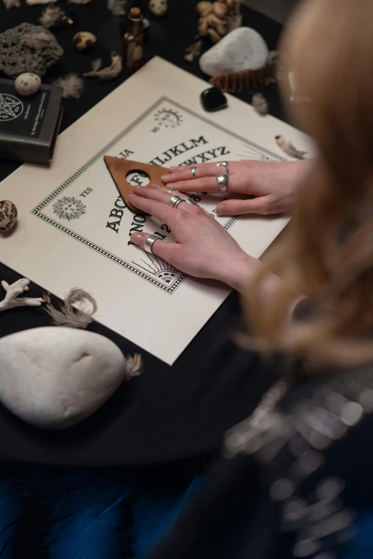 a woman sitting at a table with a book, occult inspired, crafting, 2019 trending photo, promotional image