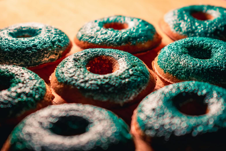 a bunch of doughnuts sitting on top of a wooden table, inspired by Elsa Bleda, trending on pexels, pop art, dark emerald mist colors, thumbnail, glitter, 33mm photo