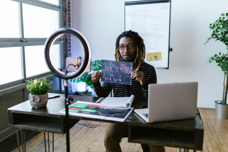 a woman sitting at a desk holding up a piece of paper, pexels contest winner, black arts movement, holding glowing laptop computer, a photo of a man, ashteroth, teaching