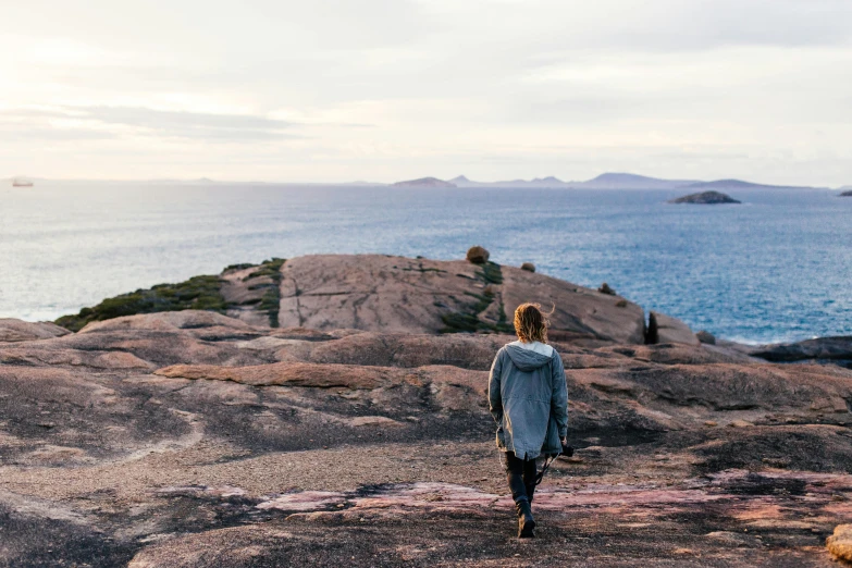 a woman standing on top of a rock next to the ocean, by Lee Loughridge, pexels contest winner, walking to the right, archipelago, aussie, casually dressed