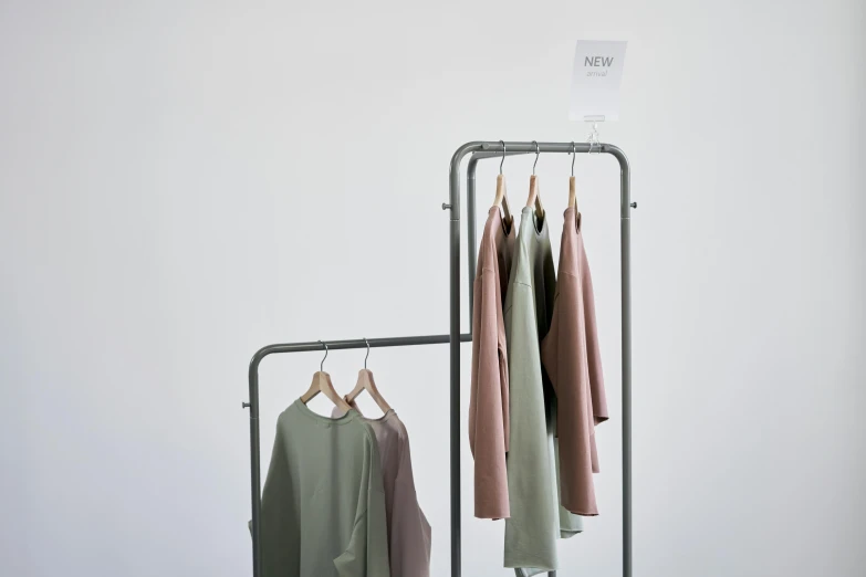 clothes hanging on a rack in front of a white wall, trending on unsplash, muted green, product display, inspect in inventory image, full dynamic colour