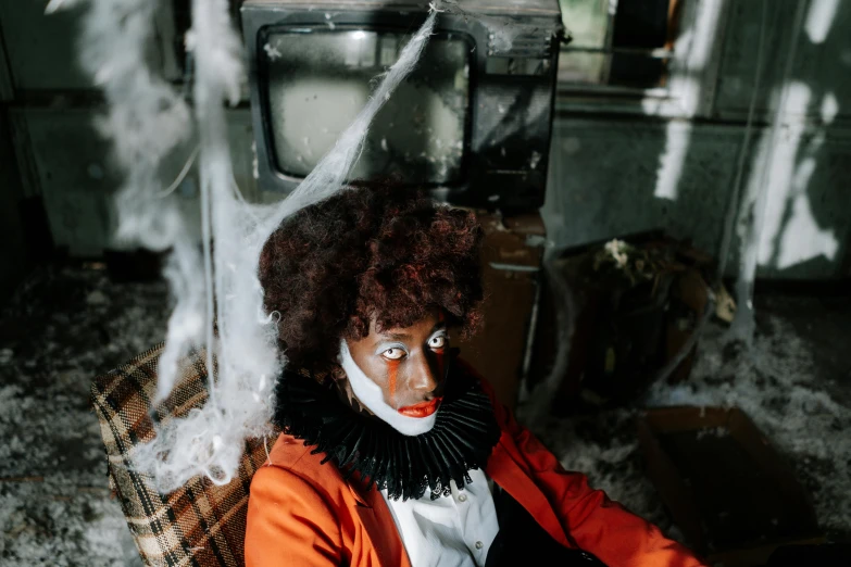 a clown sitting on a couch in front of a television, a portrait, inspired by Carrie Mae Weems, pexels contest winner, halloween decorations, in an attic, with brown skin, thumbnail