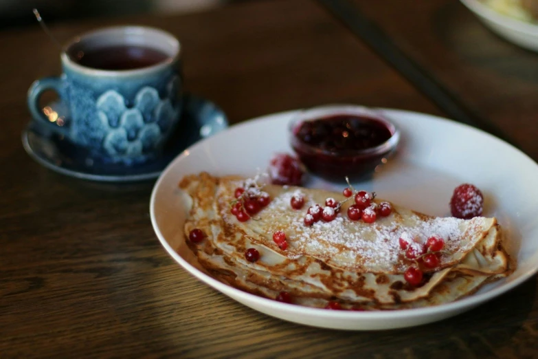 a close up of a plate of food on a table, by Alice Mason, pexels, pancakes, table in front with a cup, nordic, raspberry