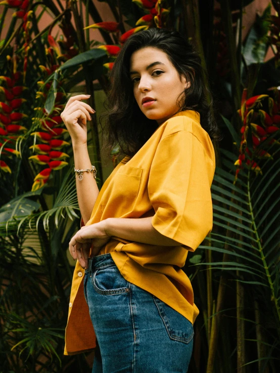 a woman standing in front of a bunch of flowers, by Robbie Trevino, gold shirt, mango, non binary model, cindy avelino