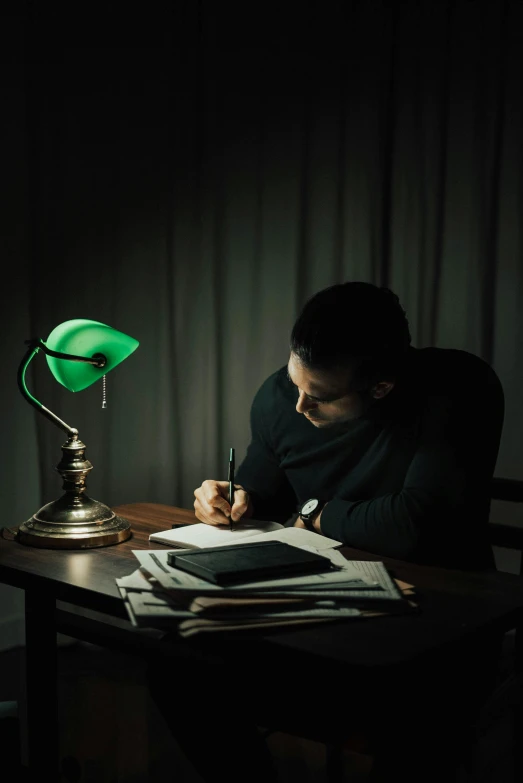 a man sitting at a desk writing in a dark room, a colorized photo, inspired by Morris Kestelman, pexels contest winner, green light, emerging from her lamp, pen and paper, a handsome