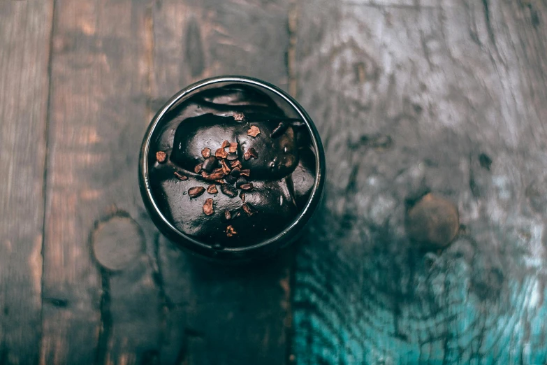 a cup of ice cream sitting on top of a wooden table, dark chocolate hair colour, top down shot, botanicals, dark. no text