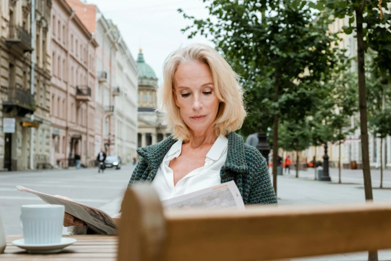 a woman sitting at a table reading a newspaper, a portrait, by Zofia Stryjenska, pexels contest winner, at a city street, middle age, avatar image, a blond