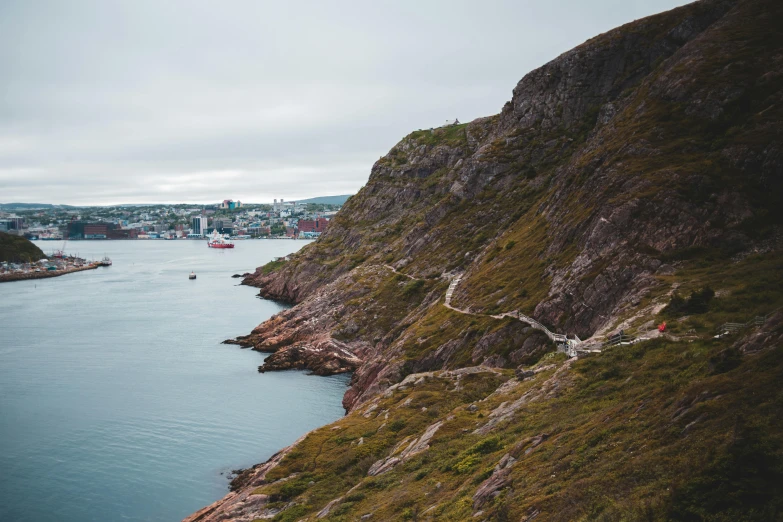 a large body of water next to a lush green hillside, a photo, pexels contest winner, les nabis, harbour in background, inuit heritage, rocky ground with a dirt path, maple syrup sea