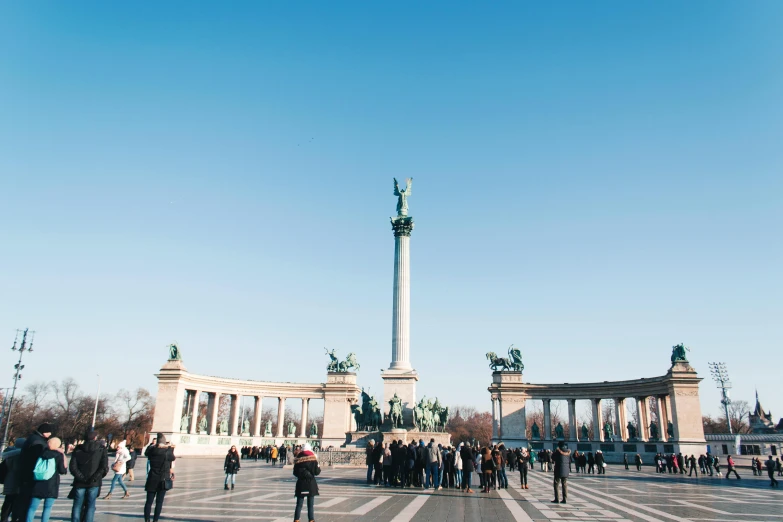 a group of people standing in front of a monument, a statue, by Thomas Häfner, pexels contest winner, art nouveau, budapest, marble columns in background, square, sunny sky