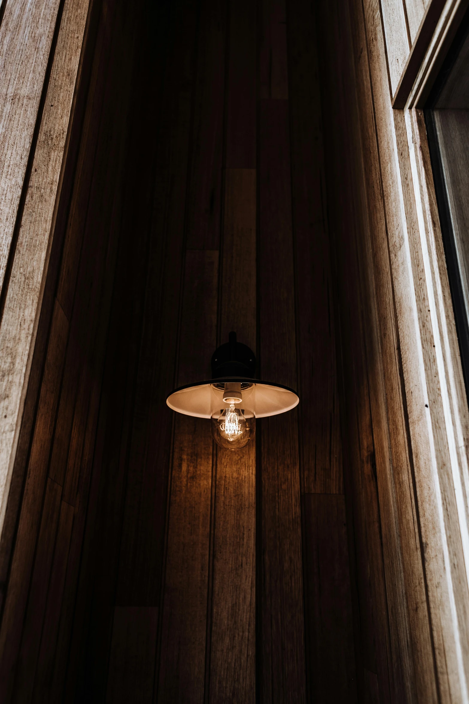 a light sitting on top of a wooden floor next to a window, by Andries Stock, unsplash, sconces, wood paneling, cafe lighting, ceiling hides in the dark