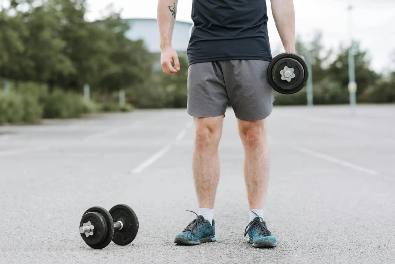 a man standing in a parking lot next to a pair of dumbbells, pexels contest winner, wearing black shorts, profile image, thumbnail, background image