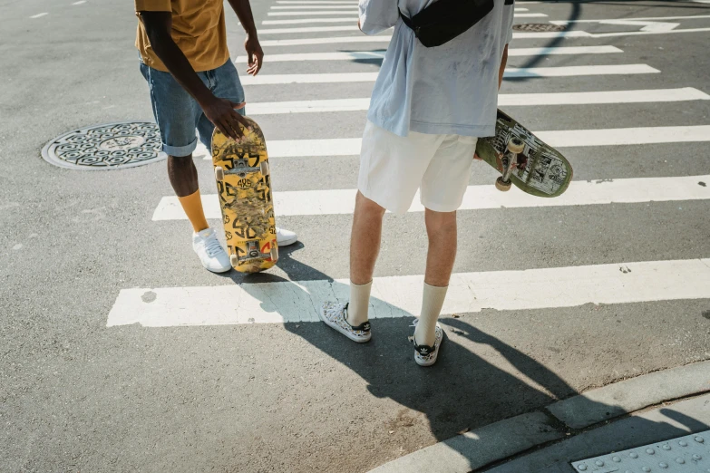 a couple of men standing next to each other on a street, pexels contest winner, detailed skateboard, white and yellow scheme, wearing shorts, crosswalks