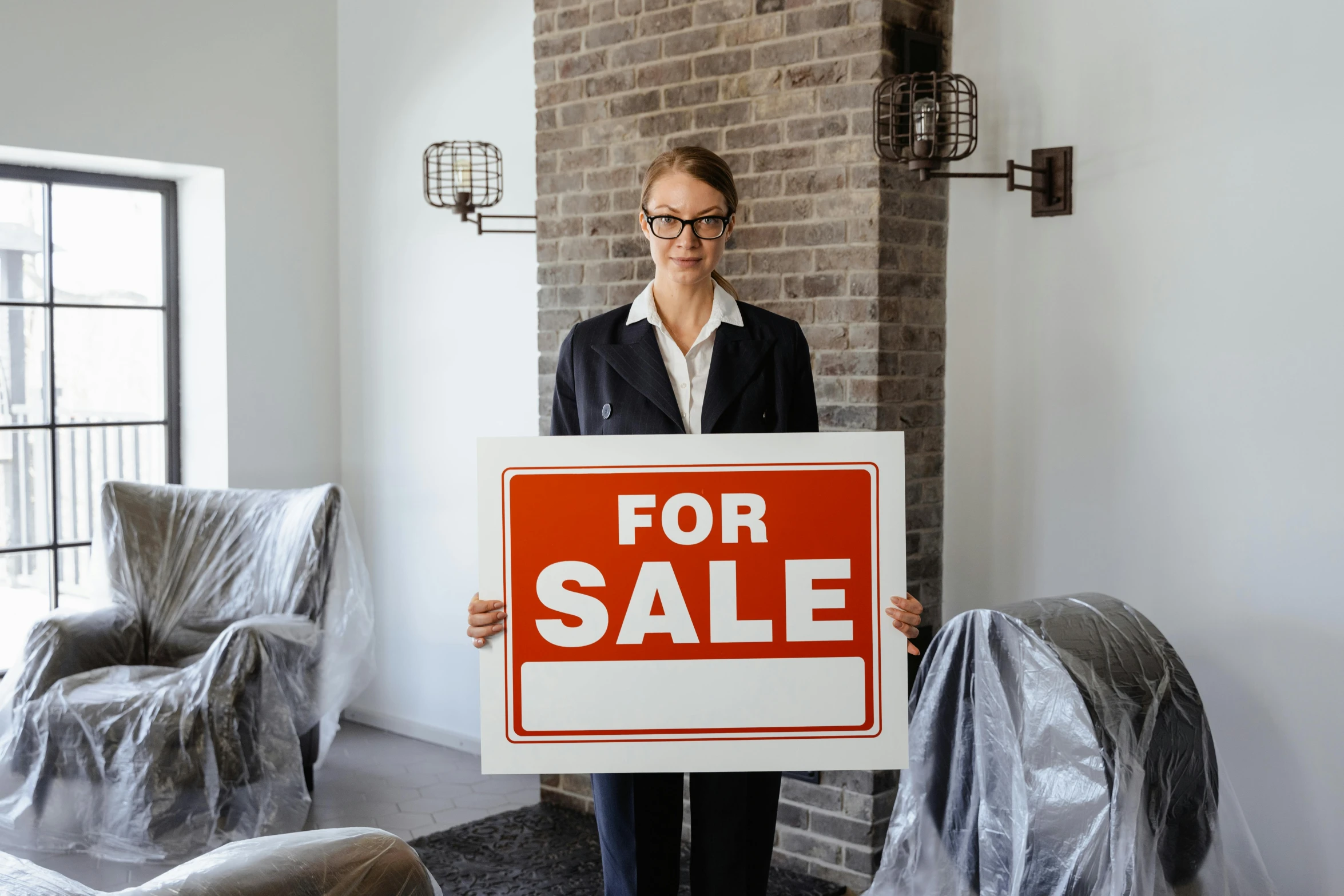 a woman holding a for sale sign in a living room, by Emma Andijewska, pexels contest winner, photorealism, in suit with black glasses, no - text no - logo, where a large, developers