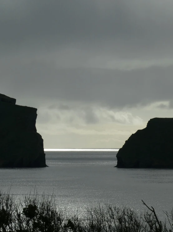 a couple of large rocks sitting on top of a body of water, inspired by Nína Tryggvadóttir, les nabis, extremely gloomy lighting, steep cliffs, seen from a distance, light coming from the entrance