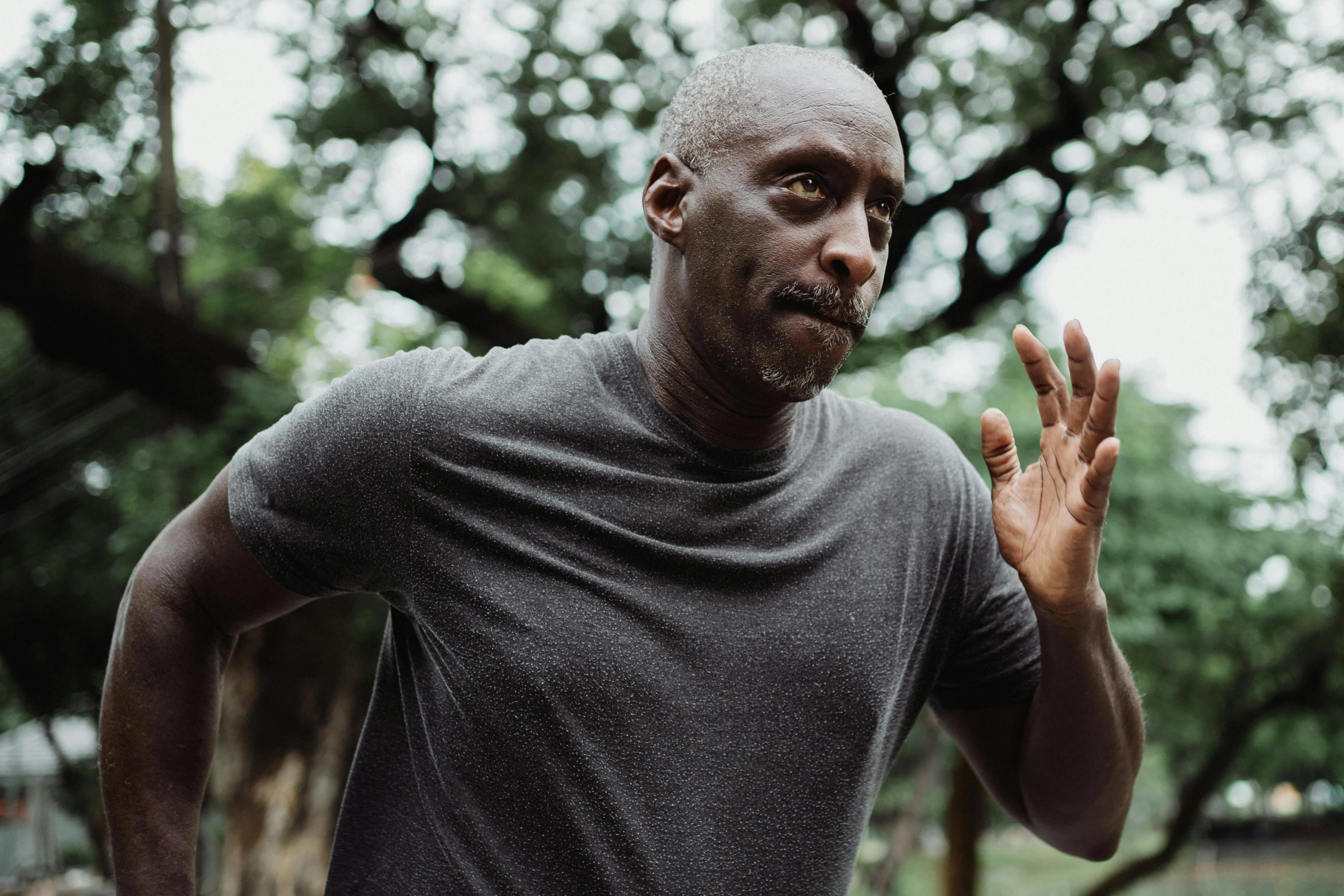 a man standing in a park with his hands in the air, inspired by Phil Foglio, pexels contest winner, happening, lance reddick, wearing a tee shirt and combats, focused gaze, distorted pose