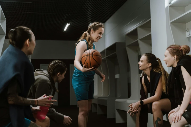 a woman in a blue dress holding a basketball, by Emma Andijewska, pexels contest winner, calmly conversing 8k, locker room, a group of people, thumbnail