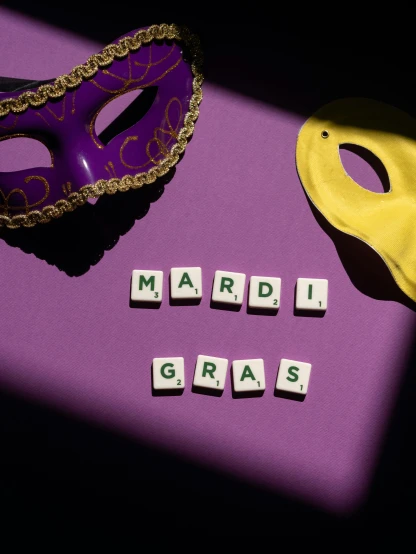 the word mardi gras spelled in scrabbles next to a purple mask, a photo, by Carey Morris, trending on pexels, visual art, made of glazed, various posed, costume, thumbnail