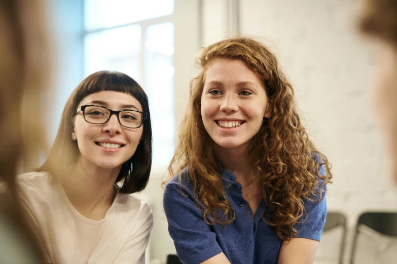 two women sitting next to each other at a table, trending on unsplash, academic art, smiling at camera, pale-skinned, close up portrait photo, avatar image