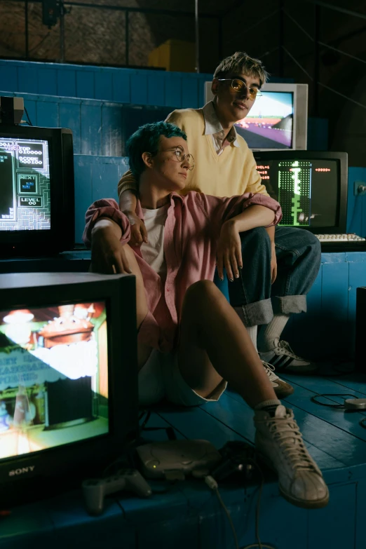 a couple of people sitting on top of a blue couch, an album cover, inspired by Liam Wong, pexels, arcade cabinet, 1 9 8 0 s computers, cyberpunk clothes, movie still
