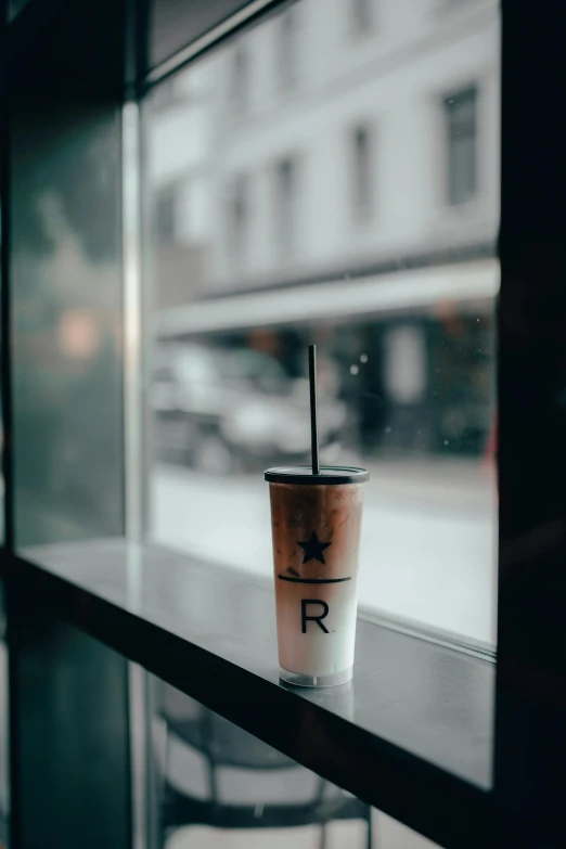 a cup of coffee sitting on top of a window sill, by Reuben Tam, unsplash contest winner, realism, iced latte, storefront, rated r, vinyl on glazing