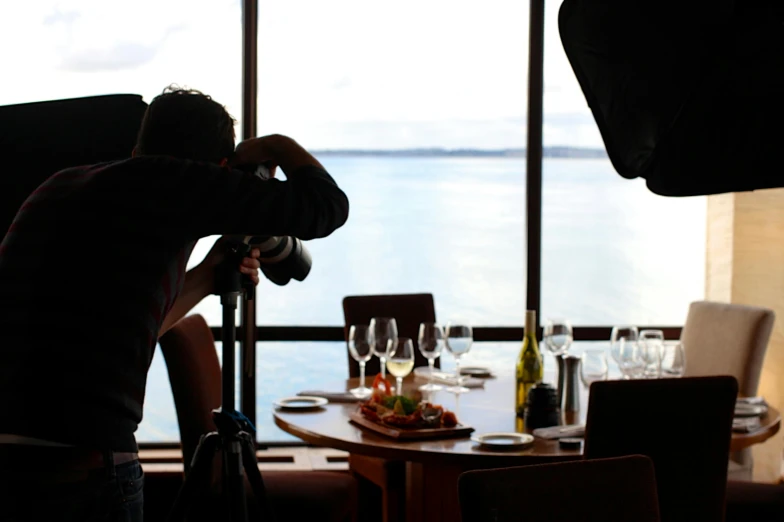 a man sitting at a table in front of a window, a picture, by Robbie Trevino, pexels contest winner, food stylist, on the ocean, tripod, standing in a restaurant