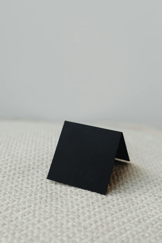 a small black square on a white surface, by Jessie Algie, unsplash, private press, folded, whole card, black furniture, metal