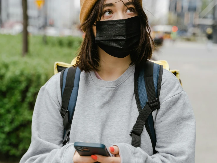 a woman wearing a face mask while looking at her phone, trending on pexels, portrait of max caulfield, japanese, student, grey